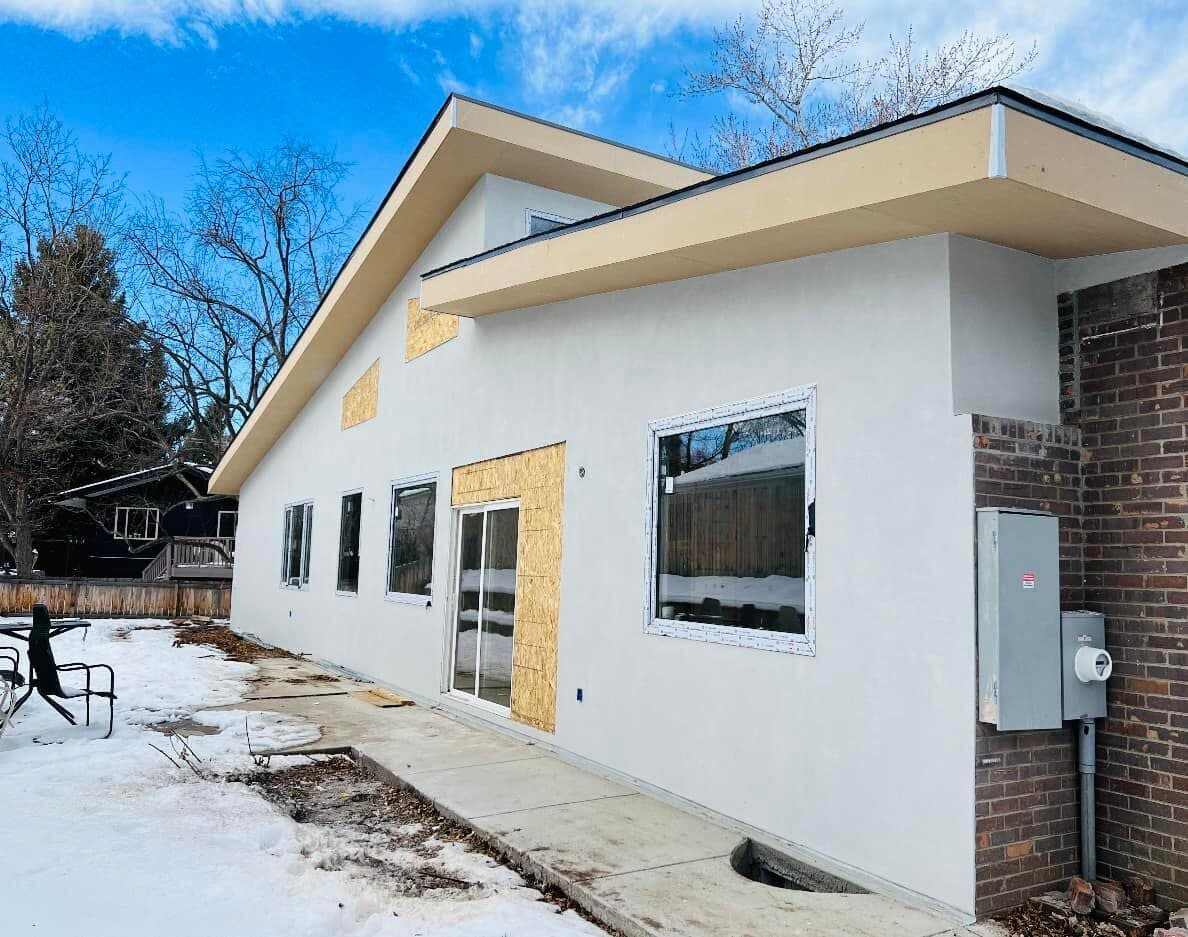 A single-storey home re-clad in bright white smooth stucco with a dark fascia, photographed in winter